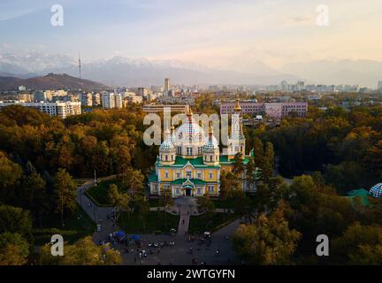 Panorama de drone aérien de la cathédrale de l'Ascension église orthodoxe russe et montagnes de neige en arrière-plan dans le parc Panfilov contre le ciel du coucher du soleil à Almat Banque D'Images