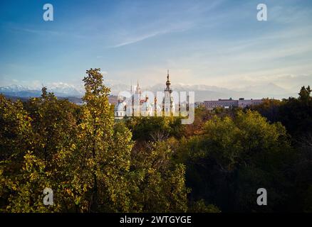 Vue aérienne par drone de la cathédrale de l'Ascension église orthodoxe russe et montagnes de neige en arrière-plan dans le parc Panfilov avec arbre au premier plan à Alma Banque D'Images