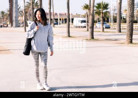 femme asiatique dans des vêtements décontractés marche avec tapis de yoga Banque D'Images