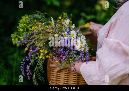 Femme tenant un panier en osier avec des fleurs de prairie. Une variété colorée de fleurs sauvages d'été. Banque D'Images