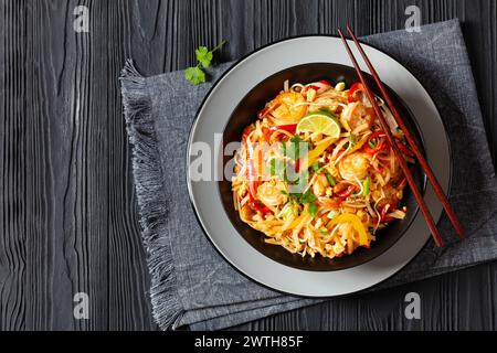 pad thai, phad thai, nouilles de riz sautées avec crevettes, cacahuètes, œufs brouillés, germes de haricots, oignons de printemps, poivron rouge et sauce dans un bol noir wit Banque D'Images