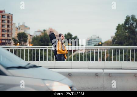 Jeune femme portant de la guitare sur son dos marchant à travers un pont urbain Banque D'Images