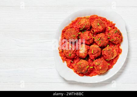Albondigas, boulettes de viande mexicaines de porc et de bœuf dans une sauce tomate à l'oignon poivron rouge saupoudrée de ciboulette sur plat blanc sur table en bois, horizontale Banque D'Images