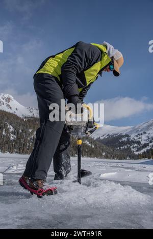 L'homme perce un trou de pêche de glace dans les montagnes du Colorado Banque D'Images