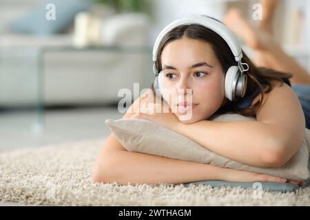Femme pensive avec casque écoutant de la musique couchée sur un tapis Banque D'Images