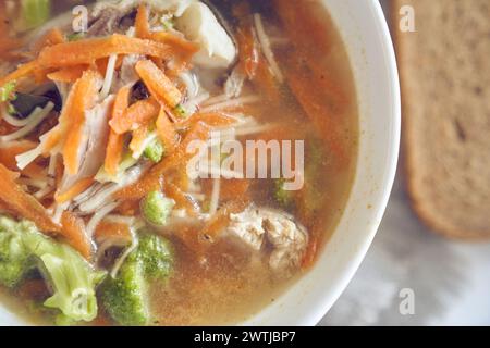 Gros plan d'une soupe saine et délicieuse de légumes et de viande dans une assiette blanche avec du pain avec espace de copie. Soupe brillante avec brocoli, carottes, morceaux de viande, servi dans une assiette. Photo de haute qualité Banque D'Images