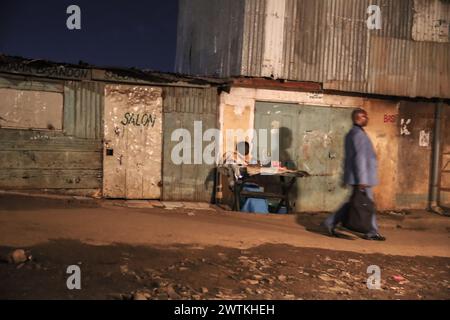 Un homme passe devant une femme vendant des légumes dans les rues du bidonville de Kibera, Nairobi. Kibera, le plus grand bidonville de Nairobi et d'Afrique, abrite plus de th Banque D'Images