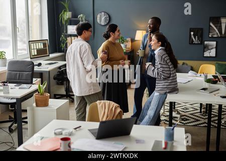 Groupe diversifié de quatre collègues joyeux dans la communication animée pendant la pause café au bureau Banque D'Images