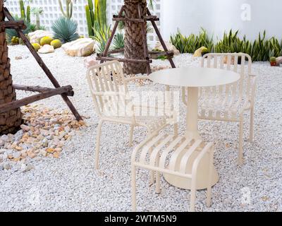 Ensemble de table minimaliste moderne, table ronde, banquette et siège de fauteuil, motif à rayures, couleur beige, matériaux en fer sur la décoration des sols en galets au tropique Banque D'Images