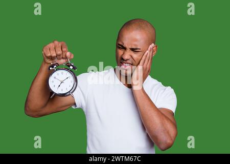 La photo en gros masculin sain peau noire il lui sa tête chauve macho perplexe tenir réveil en acier ne sais pas où couper la sonnerie wearing white t Banque D'Images