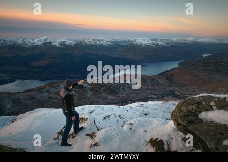 Un randonneur au sommet d'une montagne surplombe le magnifique paysage d'un lac entouré de montagnes en hiver. Loch Lomond et le parc national des Trossachs. Écosse Banque D'Images