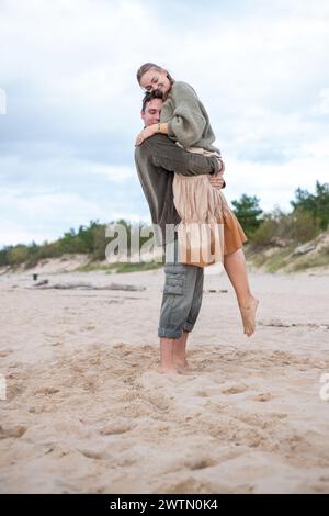 Un moment tendre entre un couple sur une plage de sable, comme un homme tient une femme proche, leur étreinte affectueuse véhiculant un sentiment de confort et de connectio Banque D'Images