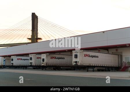 Séville, Espagne - 1er juin 2023 : plusieurs remorques XPO Logistics stationnées sur un quai de chargement avec un pont à haubans en arrière-plan, capturées au crépuscule. Banque D'Images