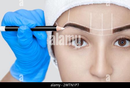 Maquillage permanent pour les sourcils de la belle femme aux sourcils épais dans le salon de beauté. Esthéticienne en gros plan faisant un sourcil tatouage. Banque D'Images