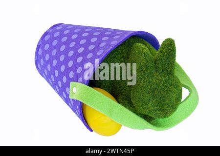 Lapin de Pâques flou vert repose par seau de panier de Pâques avec des œufs en plastique. La poignée verte est sur le récipient en feutre polkadot violet. Portez vos œufs. Banque D'Images