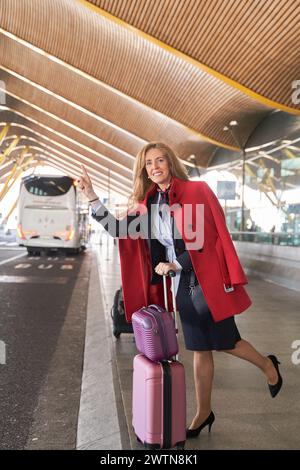 Voyageur élégant : femme d'âge moyen en manteau rouge et bagages Hails Cab pour la prochaine destination Banque D'Images