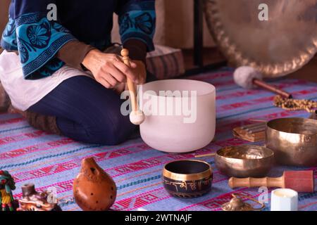 Gros plan des mains d'une femme jouant un bol chantant en quartz, tout en guidant une méditation sonore entourée d'autres instruments tels que le chant tibétain bo Banque D'Images