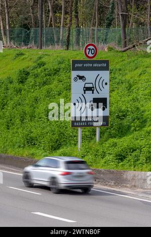 Voiture avec flou de mouvement se déplaçant devant un panneau de signalisation indiquant des contrôles de vitesse radar fréquents sur le côté d'une route française Banque D'Images