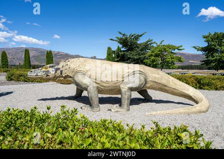 Cromwell, Nouvelle-Zélande- 3 janvier 2024 : une statue de dinosaure beige posée à mi-foulée contre le paysage de Highlands Park, avec des arbustes au premier plan Banque D'Images