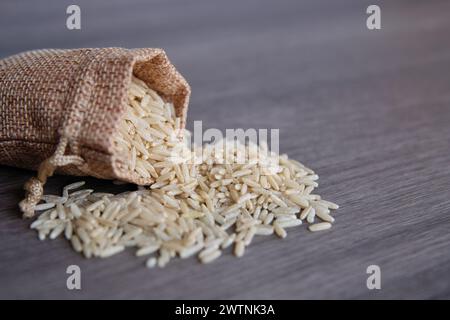 Gros plan image de riz brun dans un petit sac en toile de jute sur une table en bois avec espace de copie. Banque D'Images