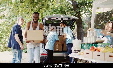 Un programme extérieur de collecte de nourriture à but non lucratif pour aider les pauvres nécessiteux et les sans-abri. Jeunes bénévoles multiethniques donnant des boîtes de dons de la voiture aux moins privilégiés. Prise de vue à main levée. Banque D'Images