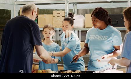 De généreux bénévoles fournissent de la nourriture et des dons aux personnes affamées et sans-abri. Lors de la collecte de nourriture, petite fille gentille et autres travailleuses caritatives distribuant des repas gratuits aux nécessiteux. Prise de vue sur trépied. Banque D'Images