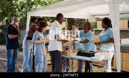 Des gens de divers horizons se rassemblent à l'extérieur pour distribuer des dons non périssables et aider les pauvres et les sans-abri. Les bénévoles multiraciaux fournissent aux personnes nécessiteuses des repas gratuits et fraîchement préparés. Banque D'Images