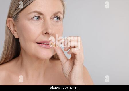 Belle femme prenant la capsule de vitamine sur fond gris, espace pour le texte Banque D'Images