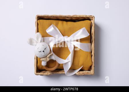 Accessoire pour bébé. Hochet et vêtements d'enfant dans une boîte en osier sur fond blanc, vue de dessus Banque D'Images