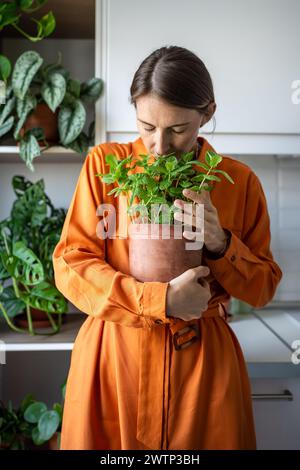 Femme avec les yeux fermés appréciant l'odeur de la plante de menthe verte sur la cuisine à la maison. Amoureux des plantes d'intérieur. Banque D'Images