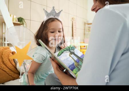 Petite fille habillée en fée avec sa mère lisant l'histoire dans la chambre Banque D'Images