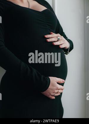 Une femme enceinte avec une coiffure et un maquillage sur son visage dans une robe serrée noire avec des tulipes blanches Banque D'Images