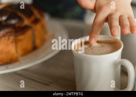 Main d'une personne tendue la main pour prendre une tasse de café chaud à la vapeur sur une table. Banque D'Images