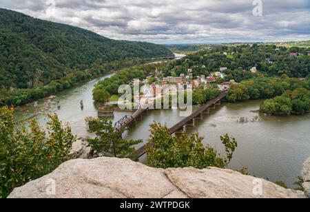 Une vue panoramique depuis une corniche de roche pâle de l'autre côté de la rivière montre deux ponts et la ville parmi les arbres verts, au Harpers Ferry National Historical Park. Banque D'Images