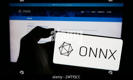 Personne tenant un smartphone avec le logo de l'écosystème ai Open Neural Network Exchange (ONNX) devant la page Web. Concentrez-vous sur l'affichage du téléphone. Banque D'Images