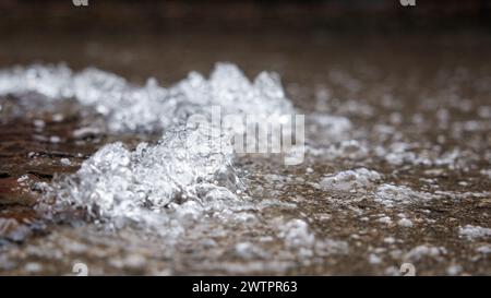 Le tuyau d'eau éclate, l'eau coule hors du trou d'homme sur l'asphalte. L'accident dans l'égout. Fuite du système d'alimentation en eau dans la ville sur le Banque D'Images