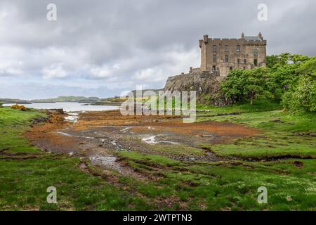 Le château de Dunvegan perché sur une falaise accidentée, surplombant un loch serein avec une palette de verts et d'aubures peignant les rives Banque D'Images