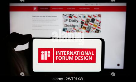 Personne tenant le téléphone portable avec le logo de l'organisation allemande International Forum Design (IF) devant la page Web de l'entreprise. Concentrez-vous sur l'affichage du téléphone. Banque D'Images