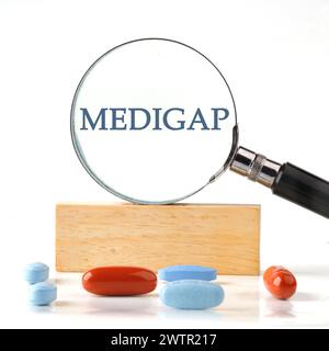 Concept médical. MEDIGAP à travers une loupe sur un bloc de bois avec des vitamines, des pilules au premier plan Banque D'Images