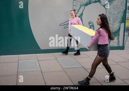 Deux femmes portent des casiers le long d'Oxford Street, le 18 mars 2024, à Londres, en Angleterre. Banque D'Images