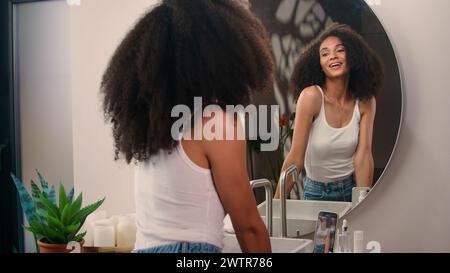 Afro-américain belle heureuse souriante jolie femme fille femelle avec cheveux bouclés choyer regardant miroir matin procédure de beauté enregistrer vidéo Banque D'Images