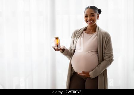 Joyeuse jeune femme noire enceinte tenant un pot avec des pilules Banque D'Images