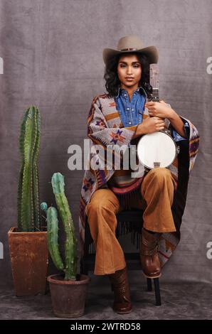 Portrait, cowgirl ou femme avec instrument pour la musique en studio et mode cool ou vêtements sur fond gris. Personne amérindienne, occidentale et Banque D'Images