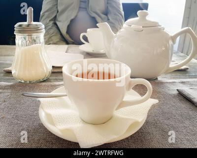 Tasse avec thé aux fruits rouges, théière et bouteille de sucre sur plateau rond en bois sur rebord de fenêtre en bois, café. Vue avant. Banque D'Images
