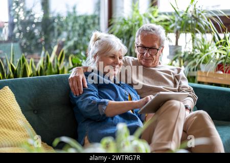 Heureux couple senior utilisant la tablette numérique tout en étant assis sur le canapé dans le salon Banque D'Images