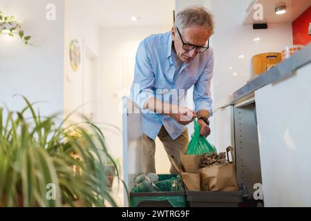 Homme senior triant les ordures dans des bacs de recyclage à la maison Banque D'Images