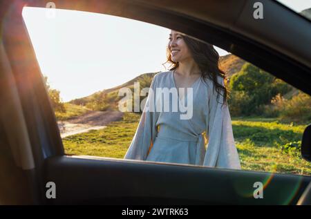 Une jeune femme asiatique attrayante sourit et profite des montagnes. Une charmante femme coréenne dans une robe de lin se détend dans la nature à l'extérieur. La vue fr Banque D'Images