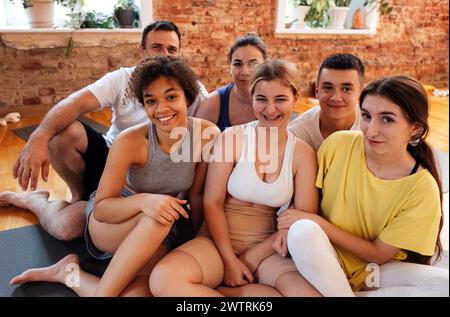 Les gens souriants multiraciaux s'assoient sur des tapis après avoir fait du yoga au club de fitness. Groupe de jeunes athlètes de différents âges et nationalités se détendre et se reposer à l'arrière Banque D'Images