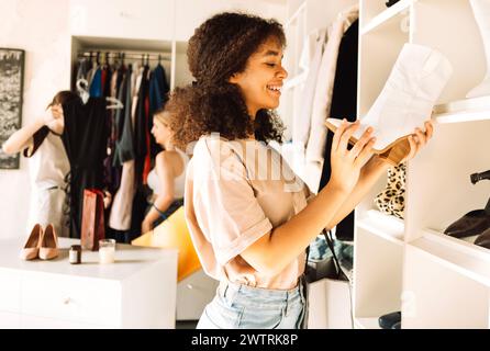 Charmantes adolescentes de différentes races choisissent des vêtements et des chaussures dans le magasin. Attrayante africaine tient la botte blanche dans ses mains et examine Banque D'Images