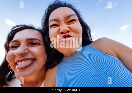 Deux filles mignonnes de différentes races grimace et amusent ensemble. Des amis multiethniques attrayants prennent des selfies drôles à l'extérieur. Gros plan d'un visage riant Banque D'Images